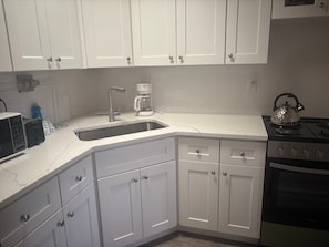 A kitchen with white cabinets, a stainless steel sink, a coffee maker, a kettle, a microwave, and a stove. - Cozy 1BR Siesta Key apartment with courtyard view (Siesta Key)