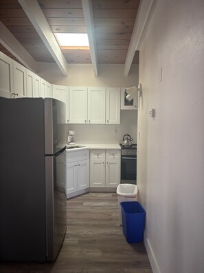 A kitchen with white cabinets, a stainless steel refrigerator, a stove, and a blue trash bin. - Cozy 1BR Siesta Key apartment with courtyard view (Siesta Key)