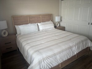 A bedroom with a wooden headboard, a large bed with white bedding, two bedside tables with lamps, and a white door in the background. - Cozy 1BR Siesta Key apartment with courtyard view (Siesta Key)