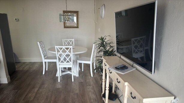 Een eethoek met een ronde tafel en witte stoelen, een aan de muur bevestigde televisie, en een houten vloer.