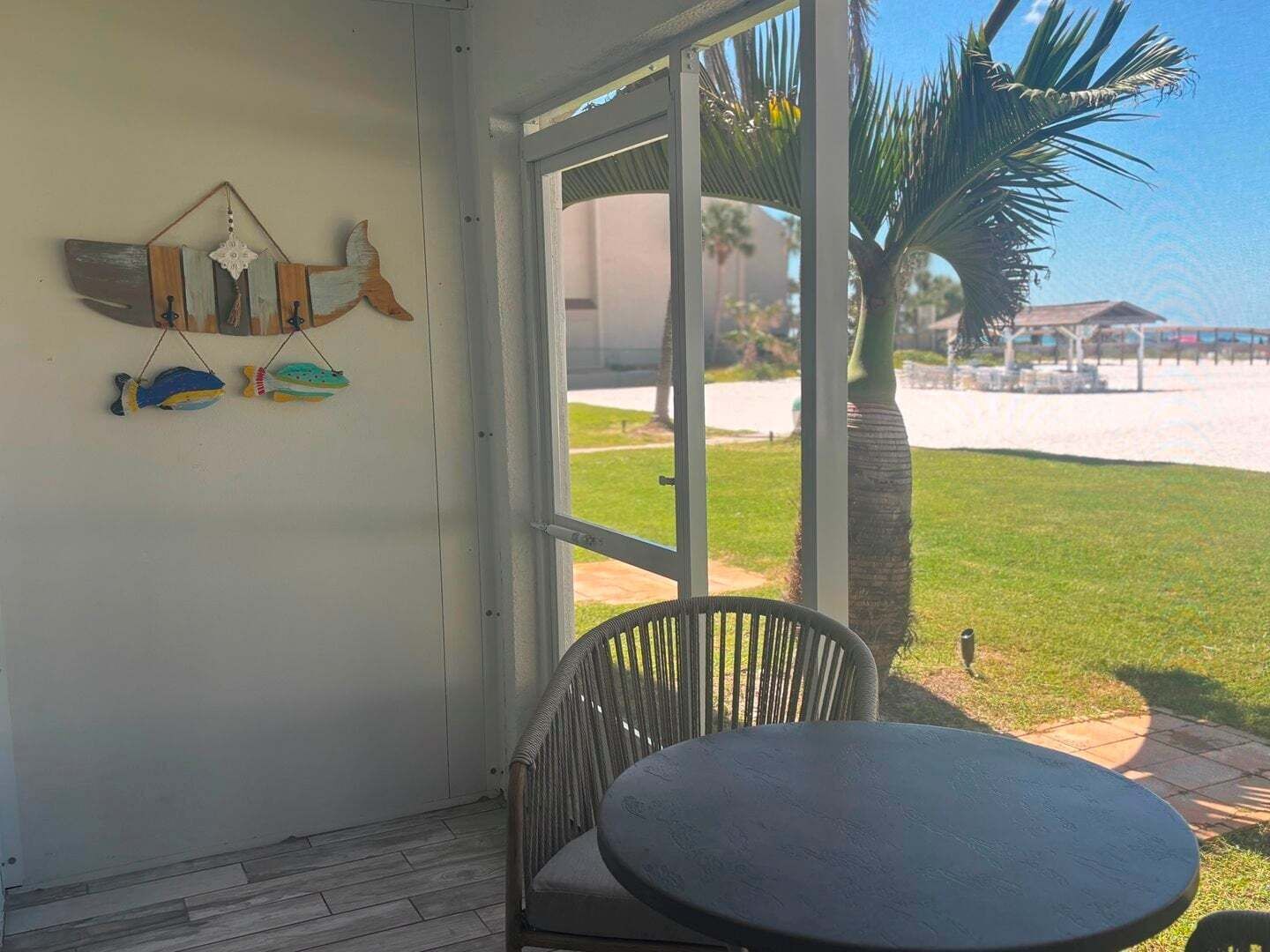 Een kamer met een glazen deur die uitkomt op uitzicht op het strand, een ronde tafel en een muur met decoratieve visfiguren.
