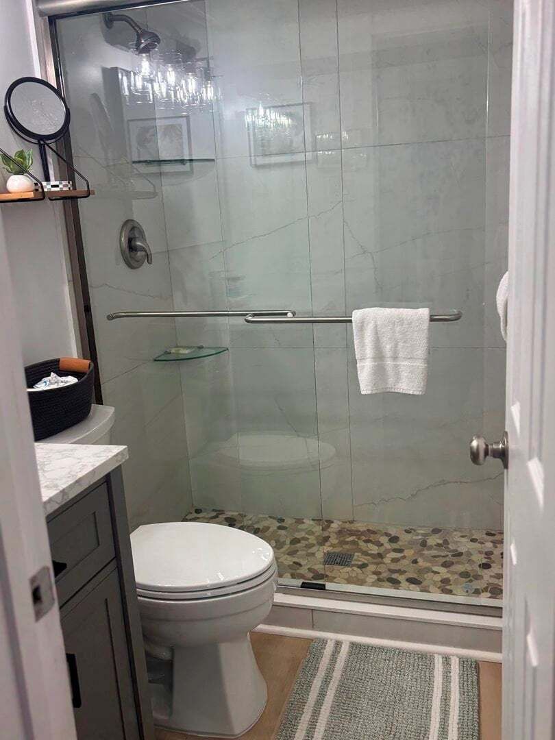 Un baño moderno con cabina de ducha de vidrio, inodoro y lavamanos con encimera de mármol.