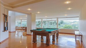 A spacious room with a pool table, large windows, and a view of greenery. - 2-bedroom Apt in Campos do Jordao Lvr0412 (Campos do Jordão)