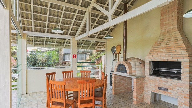 An outdoor patio with a brick oven, wooden table, and chairs. - 2-bedroom Apt in Campos do Jordao Lvr0412 (Campos do Jordão)