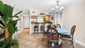 A dining area with a round table, six chairs, and a chandelier. - Pool & Palm Escape – Unit C208 (Biloxi)