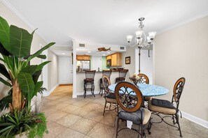 A dining area with a round table, six chairs, and a chandelier. - Pool & Palm Escape – Unit C208 (Biloxi)