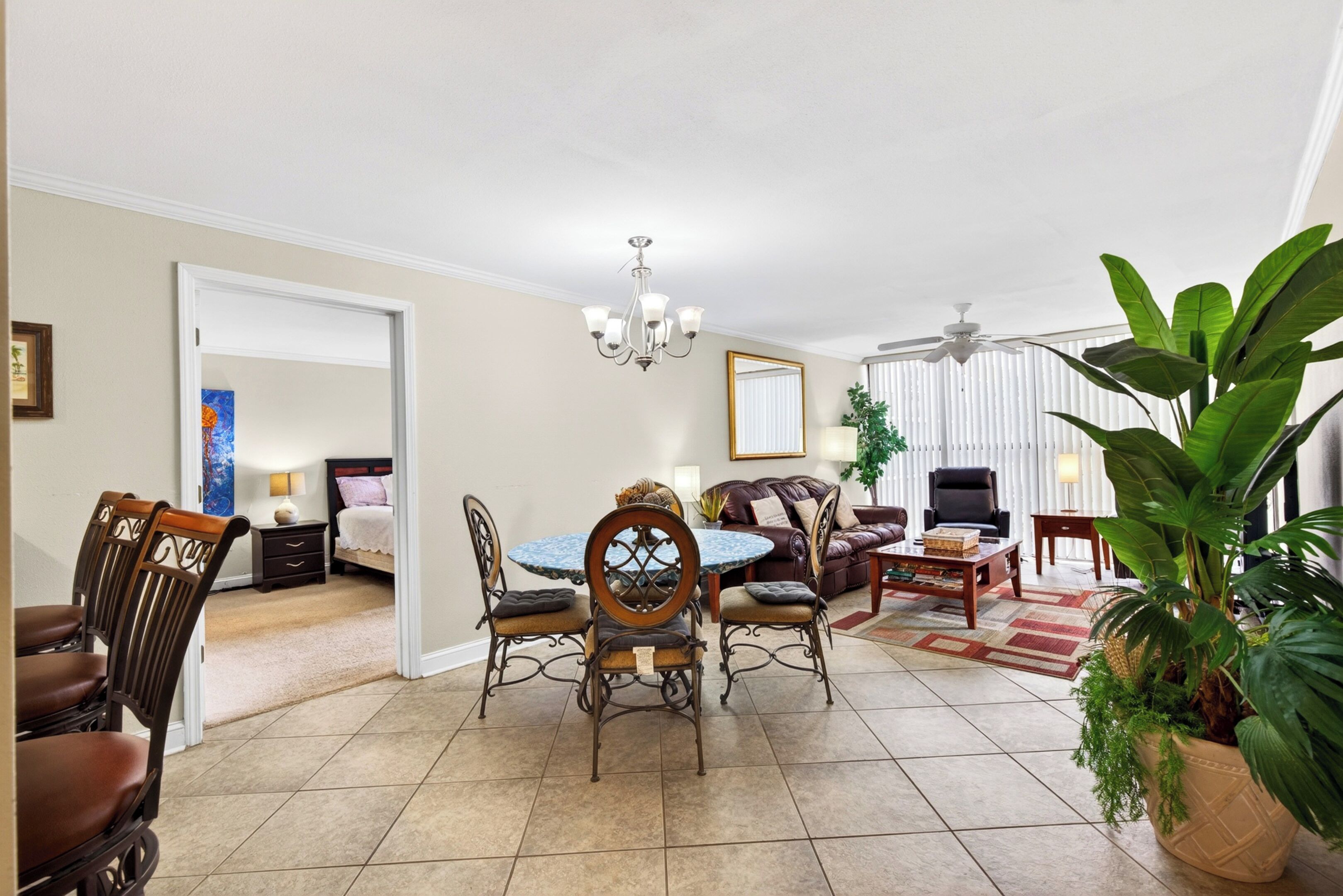 A spacious living area with a dining table, chairs, a sofa, a coffee table, and a large potted plant.