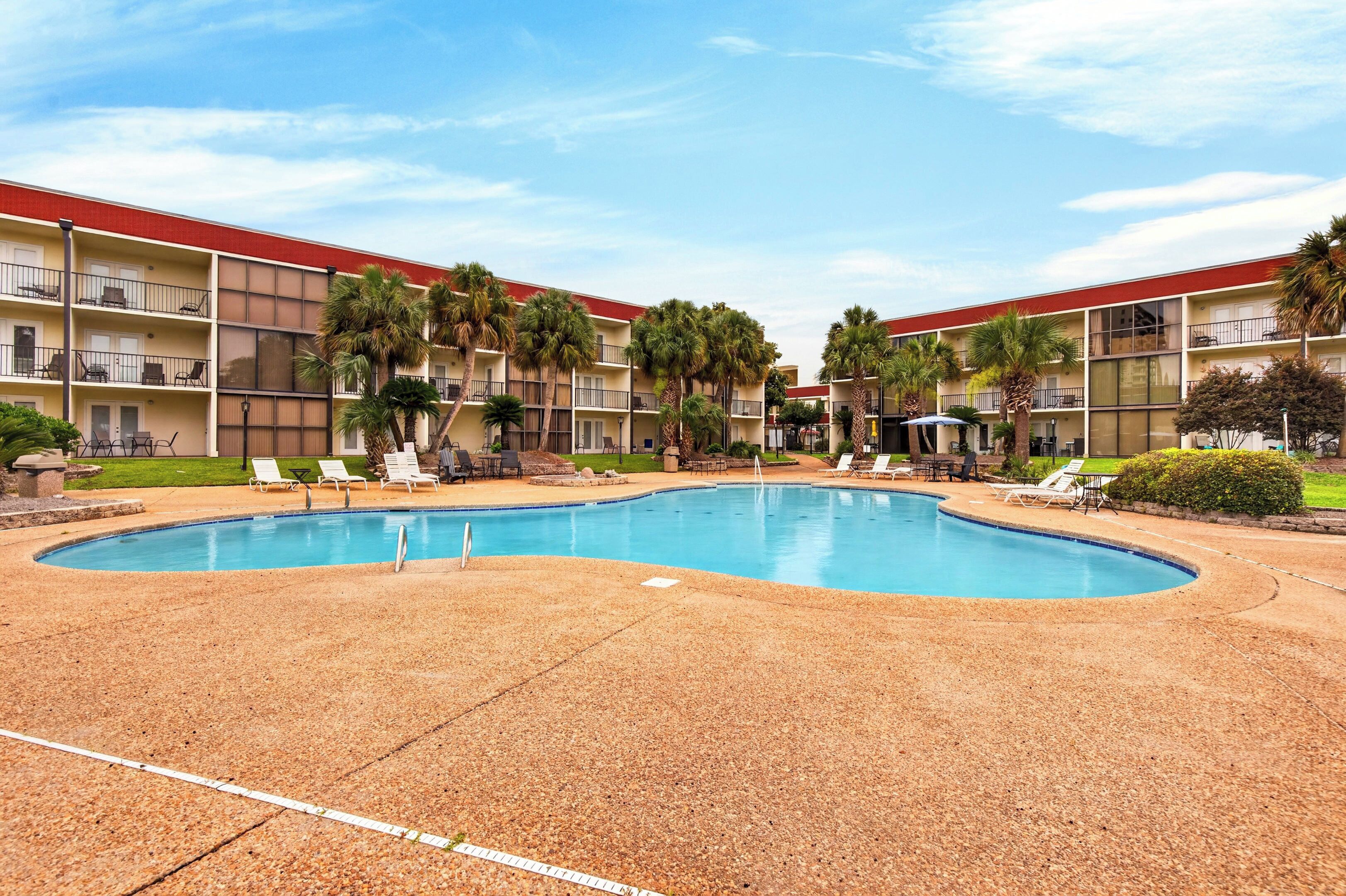 A hotel with a swimming pool, multiple balconies, and palm trees.