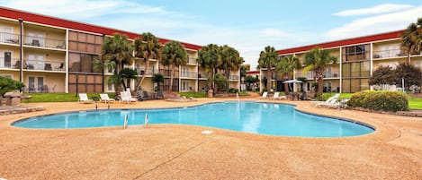 A hotel with a swimming pool, multiple balconies, and palm trees.