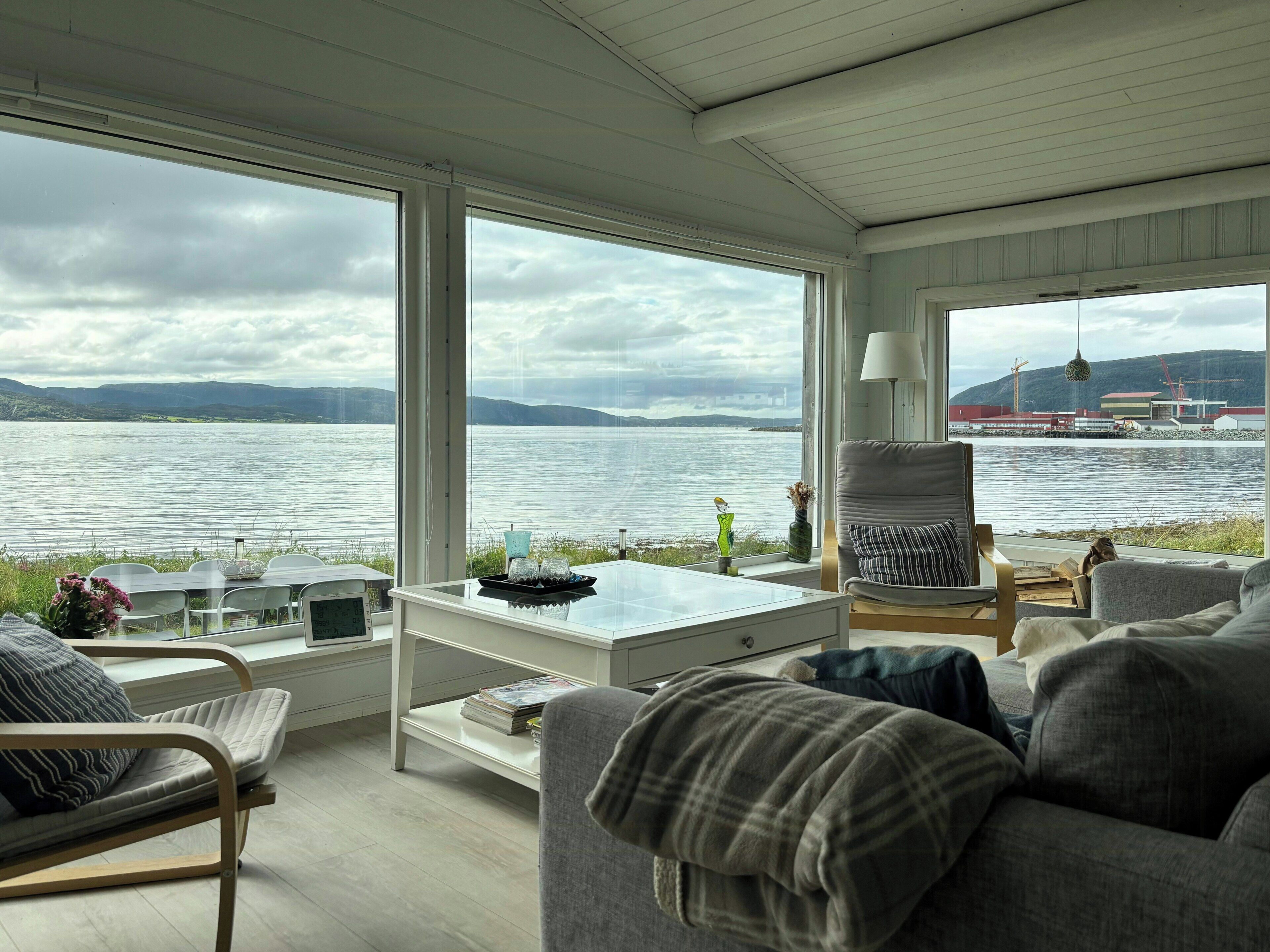 A modern living room with a large window overlooking a lake, a sofa, a coffee table, and a chair.