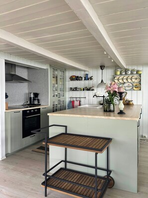 A kitchen with a central island, a stove, cabinets, and a hanging light fixture.