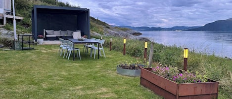 A lakeside outdoor seating area with a table and chairs, a built-in bench, and a flower bed.