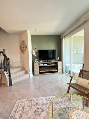 A modern living room with a flat-screen TV, a fireplace, a staircase, and a glass coffee table. - Modern Palm Coast Townhome, Office, Pet-Friendly, Fenced-in Turf Yard (Palm Coast)