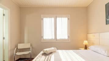 A hotel room with a bed, a chair, a window, and a nightstand with a lamp.