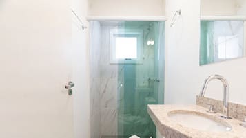 Un baño con cabina de ducha de vidrio, un lavamanos con encimera de mármol y un espejo sobre el lavamanos.