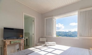 Habitació d'hotel amb llit, televisió sobre un suport de fusta, bany amb dutxa i finestra amb vista a la muntanya.