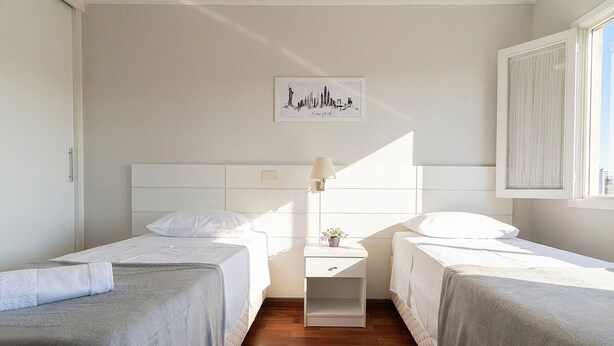 A hotel room with two beds, a nightstand with a lamp, a wall-mounted artwork, and a window with curtains. - Apt in Condo w/ BBQ in Capivari Lvr0017 (Campos do Jordão)