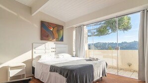 A bedroom with a bed, a bedside table, a painting, and a view of the outdoors. - Apt in Condo w/ BBQ in Capivari Lvr0017 (Campos do Jordão)