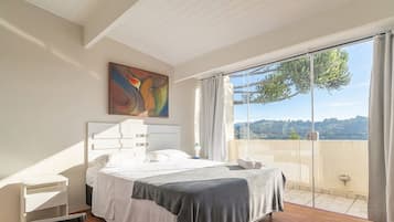 A bedroom with a bed, a bedside table, a painting, and a view of the outdoors.