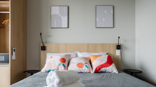 Ein Hotelzimmer mit einem Bett, zwei Nachttischen, einem hölzernen Kopfteil und zwei an der Wand befestigten Kunstwerken.