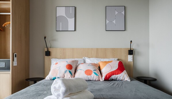 Ein Hotelzimmer mit einem Bett, zwei Nachttischen, einem hölzernen Kopfteil und zwei an der Wand befestigten Kunstwerken.