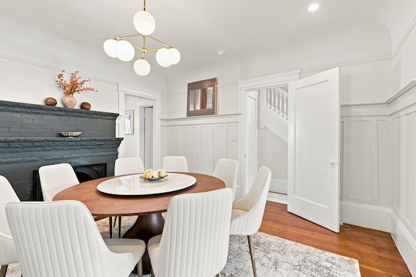 A dining area with a round table, white chairs, a fireplace, and a staircase.