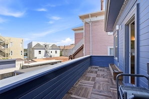 A balcony with a view of neighboring buildings, a wooden floor, and a metal railing.