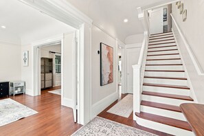 A spacious hallway with a wooden staircase, white walls, and a large abstract painting.