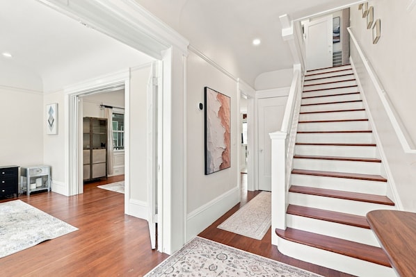 A spacious hallway with a wooden staircase, white walls, and a large abstract painting. - Restored Lake Merritt Victorian Retreat (Oakland)