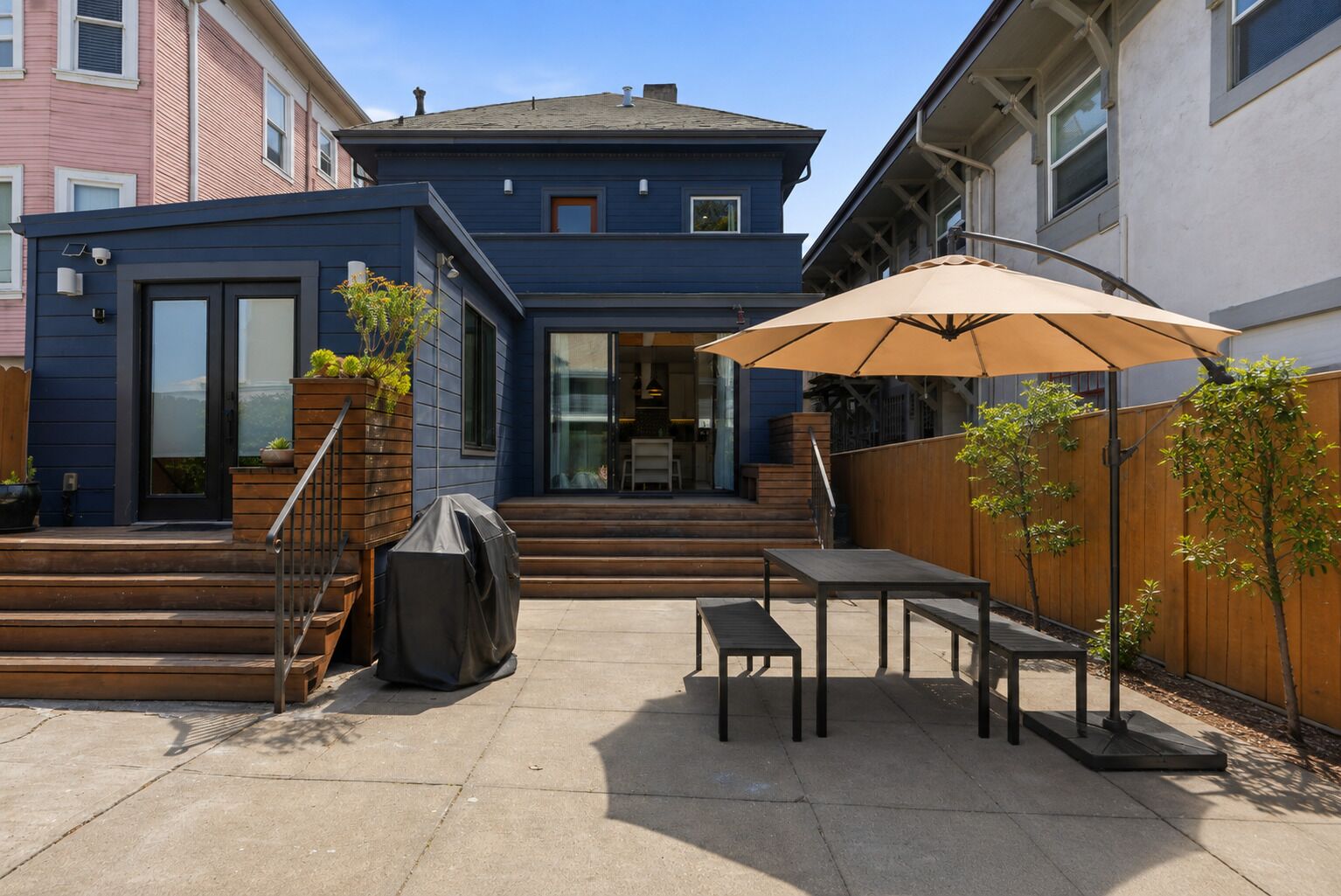 Un jardin à l’arrière d’une maison, avec une terrasse, un barbecue et une clôture en bois.
