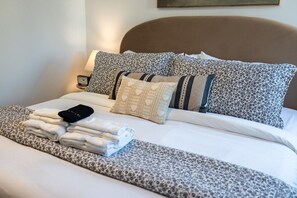 Un lit bien fait, avec un téléphone intelligent, des serviettes pliées et des coussins à motifs.