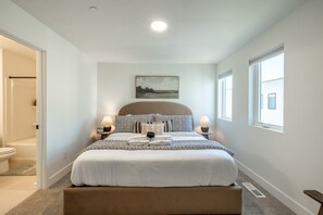 Een slaapkamer met een bed, nachtlampjes, een schilderij en een raam.