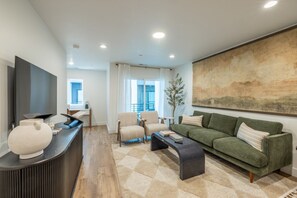 Een moderne woonkamer met een flatscreen televisie, een bank, fauteuils, een salontafel en een groot abstract schilderij aan de muur.