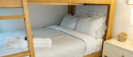A bunk bed with a wooden headboard, a bedside table with a basket, and neatly folded towels.