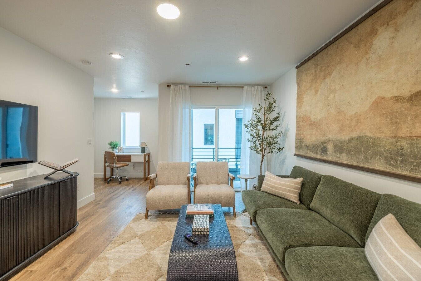 Un salon moderne avec un téléviseur à écran plat, un canapé, deux fauteuils, une table basse et un tableau accroché au mur.