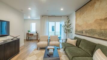 Un salon moderne avec un téléviseur à écran plat, un canapé, deux fauteuils, une table basse et un tableau accroché au mur.