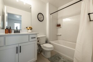 Een badkamer met toilet, wastafel met toiletartikelen, douche en handdoekhouder.