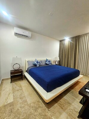 Una habitación de hotel con una cama, dos mesitas de noche, una lámpara, un equipo de aire acondicionado y una cortina.