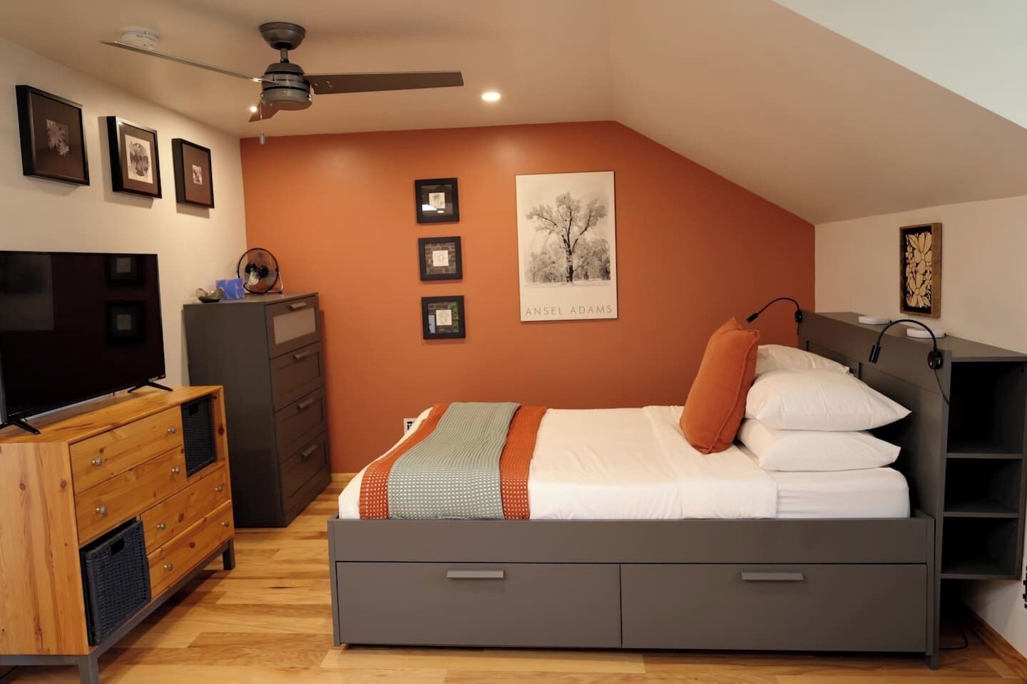 A bedroom with a bed, dresser, TV, and artwork on the walls.