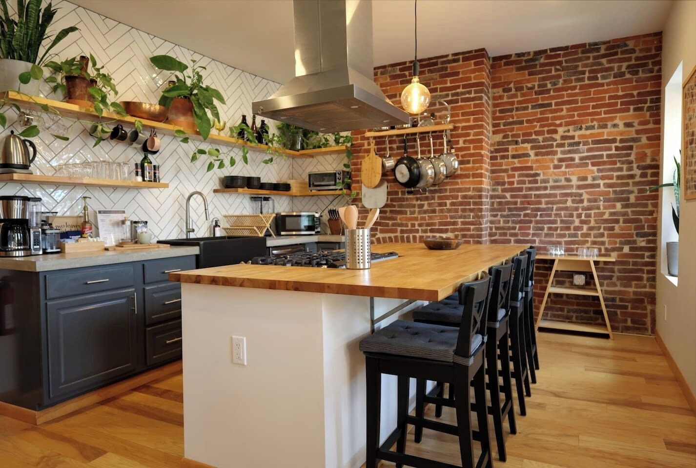 A modern kitchen with a central island, dark cabinetry, and a brick wall.