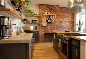 Una cocina con pared de ladrillo, estantes de madera, estufa y una percha para ollas.