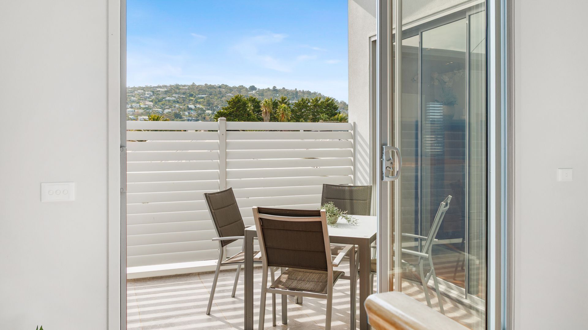 A balcony with a table and chairs, a glass door, and a view of a hillside.