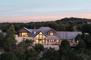 Una casa moderna de dos pisos amb grans finestres i un teulat inclinat, envoltada de vegetació densa.