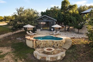 A backyard with a swimming pool, lounge chairs, and a covered seating area.
