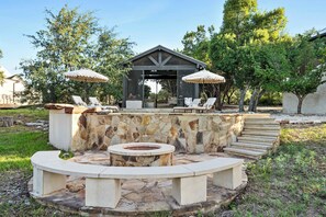 Un espace extérieur aménagé en pierre avec un foyer, des fauteuils et des parasols.
