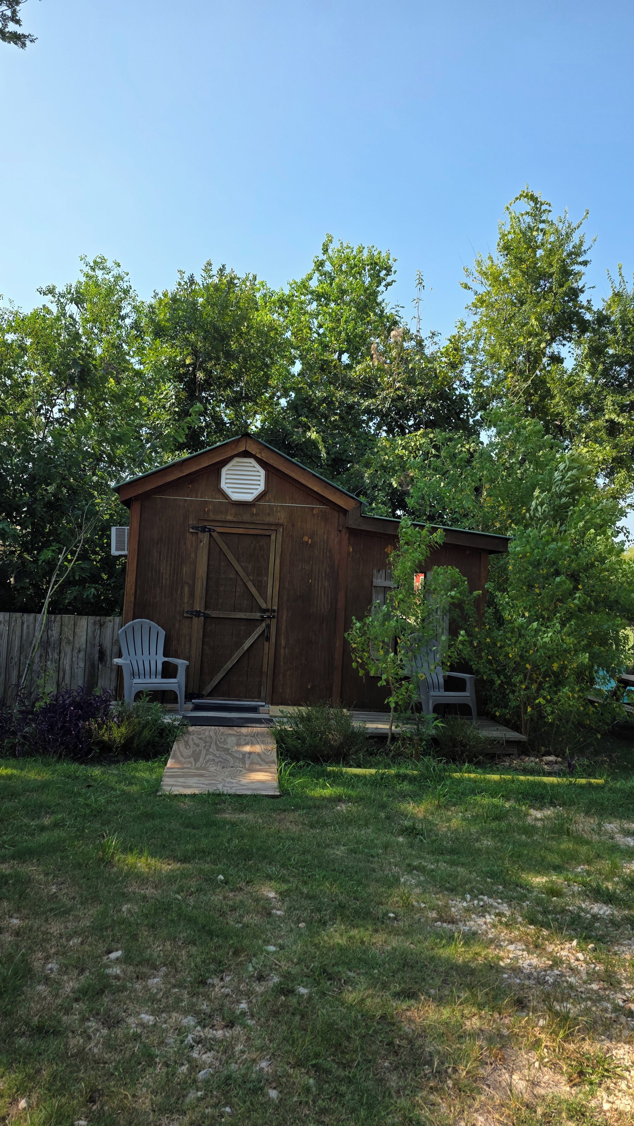 A wooden shed with a large door, a small porch, and a chair outside.