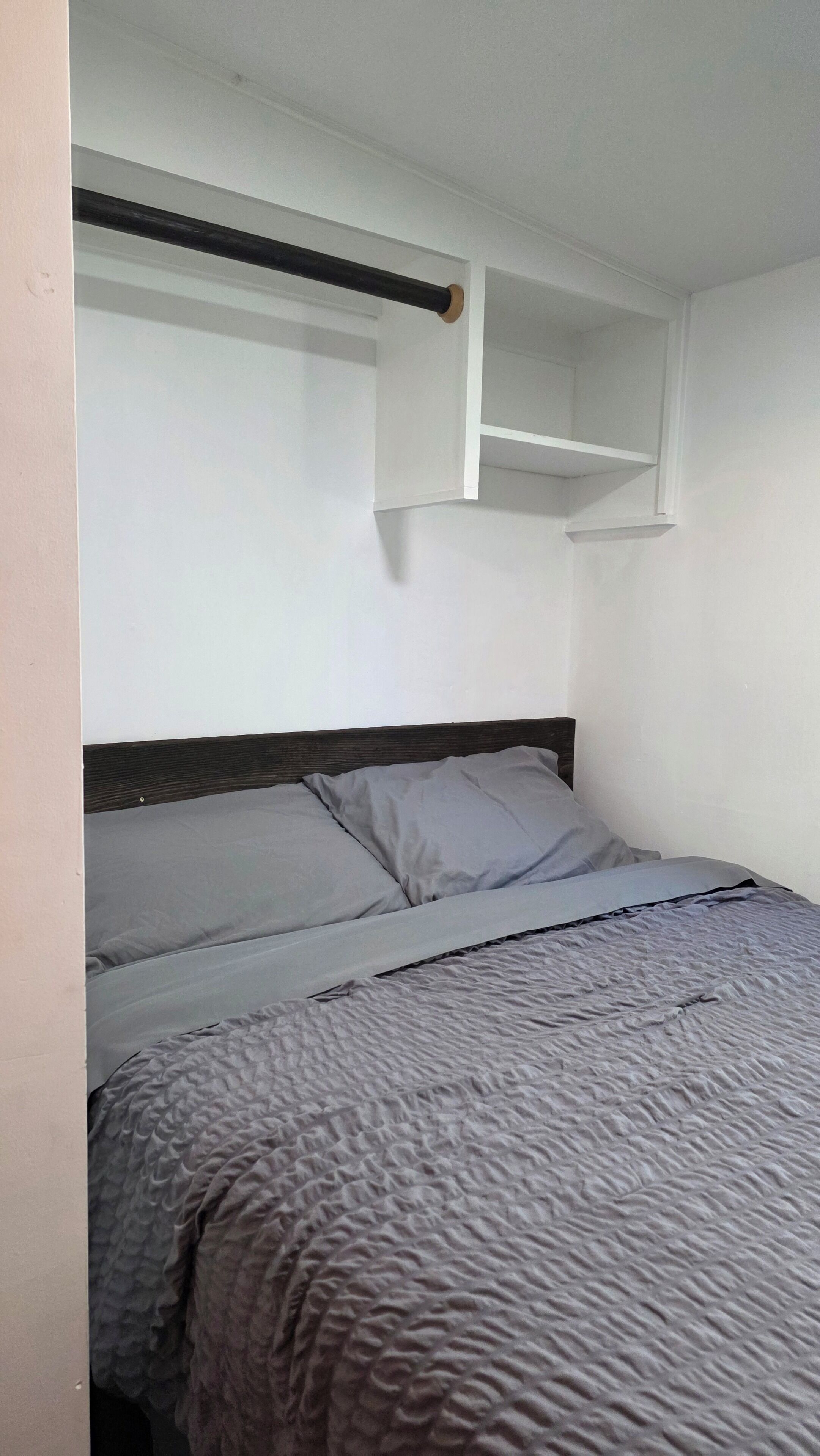 A bedroom with a bed, a headboard, and a shelf above the bed.