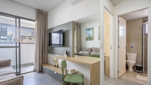 A modern hotel room with a large window, a flat-screen TV, a wooden desk, a green chair, a sofa, and a bathroom with a toilet and bidet. - Full Apt 250m From Paulista Metro Station Nxo1402 (São Paulo)
