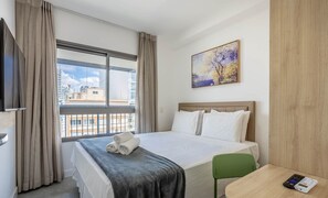 Ein Hotelzimmer mit Bett, einem Gemälde, einem Fenster mit Vorhängen und Blick auf Gebäude.