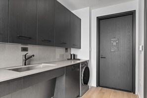 Une cuisine moderne avec des meubles de couleur sombre, un évier en acier inoxydable et un lave-linge encastré.